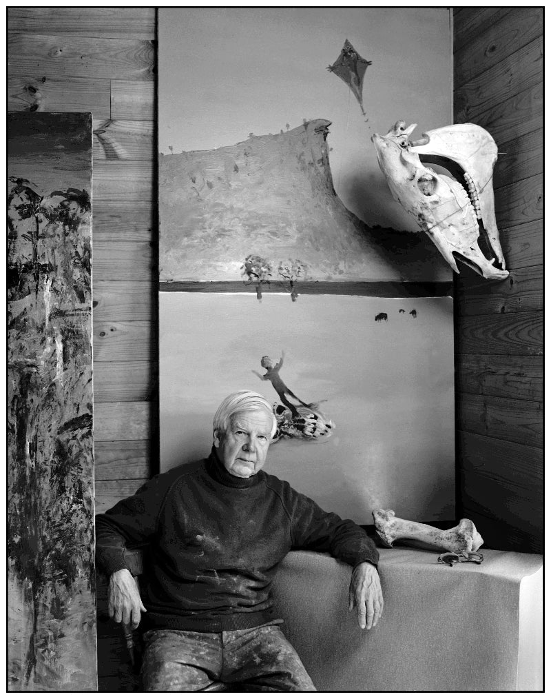 Man sitting in front of a wall with various artworks and sculptures.